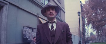 Movie still from “Neruda” (2016), directed by Pablo Larraín – A man in a suit and hat standing in front of a building; Medium shot, Low angle
