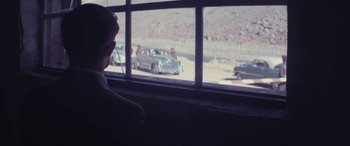 Movie still from “Neruda” (2016), directed by Pablo Larraín – A man sitting on a bench looking out of a window at cars; Medium shot, High angle