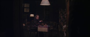 Movie still from “Neruda” (2016), directed by Pablo Larraín – A woman sitting at a table in a dark room; Wide shot, High angle