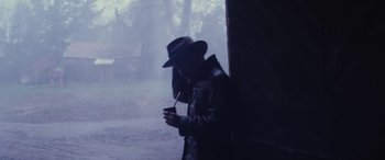 Movie still from “Neruda” (2016), directed by Pablo Larraín – A man in a black hat smoking a cigarette in front of a tree; Medium shot, Low angle