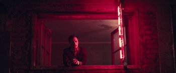 Movie still from “Neruda” (2016), directed by Pablo Larraín – A man sitting on a ledge in a dark room; Medium shot, Low angle