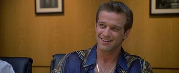 Movie still from “Never Been Kissed” (1999), directed by Raja Gosnell – A man smiling for the camera while sitting in a chair; Close Up shot, Over the shoulder angle