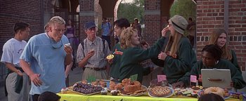 Movie still from “Never Been Kissed” (1999), directed by Raja Gosnell – A group of people standing next to a table of food; Medium shot, Over the shoulder angle