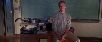 Movie still from “Never Been Kissed” (1999), directed by Raja Gosnell – A man sitting in front of a chalkboard in a classroom; Medium shot, Over the shoulder angle