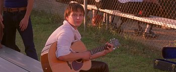 Movie still from “Never Been Kissed” (1999), directed by Raja Gosnell – A young man sitting in the grass with a guitar; Medium shot, Low angle