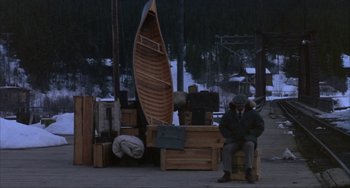 Movie still from “Never Cry Wolf” (1983), directed by Carroll Ballard – A man sitting next to a wooden boat on a dock; Wide shot, High angle