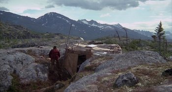 Movie still from “Never Cry Wolf” (1983), directed by Carroll Ballard – A man standing in front of a hut in the mountains; Extreme Wide shot, High angle
