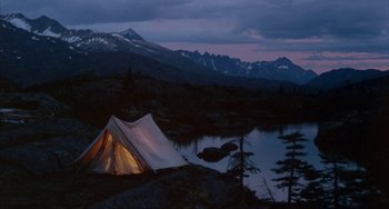 Movie still from “Never Cry Wolf” (1983), directed by Carroll Ballard – A tent is lit up by the light of a campfire at dusk; Extreme Wide shot, High angle
