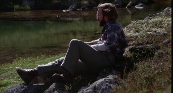 Movie still from “Never Cry Wolf” (1983), directed by Carroll Ballard – A man sitting on a rock near a body of water; Wide shot, High angle
