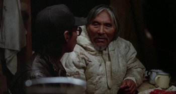Movie still from “Never Cry Wolf” (1983), directed by Carroll Ballard – A man with a hat and glasses talking to another man; Medium shot, Over the shoulder angle