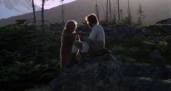 Movie still from “Never Cry Wolf” (1983), directed by Carroll Ballard – Two people sitting on top of a large rock in the woods; Wide shot, Over the shoulder angle