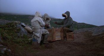 Movie still from “Never Cry Wolf” (1983), directed by Carroll Ballard – A group of people sitting around a wooden crate; Wide shot, High angle