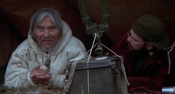Movie still from “Never Cry Wolf” (1983), directed by Carroll Ballard – A man sitting next to another man in front of a tent; Medium shot, High angle