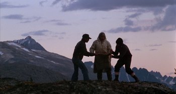 Movie still from “Never Cry Wolf” (1983), directed by Carroll Ballard – Three people standing on top of a hill with mountains in the background; Wide shot, High angle