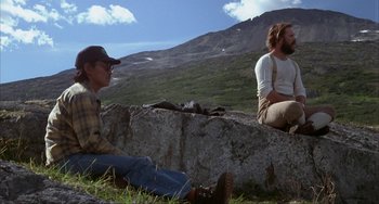 Movie still from “Never Cry Wolf” (1983), directed by Carroll Ballard – Two people sitting on a rock in a field; Wide shot, Low angle