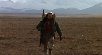 Movie still from “Never Cry Wolf” (1983), directed by Carroll Ballard – A man walking through a field with a rifle strapped to his back; Wide shot, Low angle