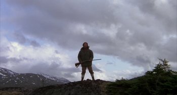 Movie still from “Never Cry Wolf” (1983), directed by Carroll Ballard – A man standing on top of a hill holding a rifle; Wide shot, Low angle