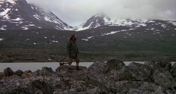 Movie still from “Never Cry Wolf” (1983), directed by Carroll Ballard – A man walking on top of a rock in front of a mountain; Wide shot, High angle