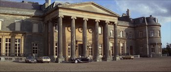 Movie still from “Never Say Never Again” (1983), directed by Irvin Kershner – An old car parked in front of a large building; Extreme Wide shot, Low angle