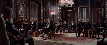 Movie still from “Never Say Never Again” (1983), directed by Irvin Kershner – A group of men and women sitting in chairs in front of a chandelier; Wide shot, High angle