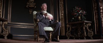 Movie still from “Never Say Never Again” (1983), directed by Irvin Kershner – An older man sitting in a chair holding a cat; Medium shot, Low angle