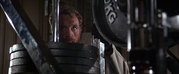 Movie still from “Never Say Never Again” (1983), directed by Irvin Kershner – A man with a beard is looking at a weight; Close Up shot, Low angle