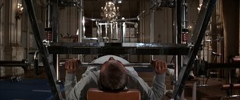 Movie still from “Never Say Never Again” (1983), directed by Irvin Kershner – A man is lifting a barbell in a gym; Medium shot, Low angle
