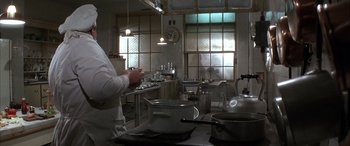 Movie still from “Never Say Never Again” (1983), directed by Irvin Kershner – A person standing in a kitchen preparing a meal; Medium shot, Low angle