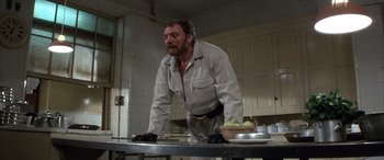 Movie still from “Never Say Never Again” (1983), directed by Irvin Kershner – A man standing at a table in a kitchen; Medium shot, Low angle