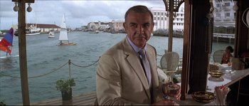 Movie still from “Never Say Never Again” (1983), directed by Irvin Kershner – A man in a suit and tie holding a glass of wine; Medium shot, Low angle