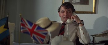 Movie still from “Never Say Never Again” (1983), directed by Irvin Kershner – A man talking on a phone while wearing a british flag hat; Close Up shot, Low angle