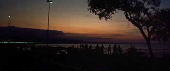 Movie still from “Never Say Never Again” (1983), directed by Irvin Kershner – A group of people standing next to a body of water at night; Extreme Wide shot, Low angle