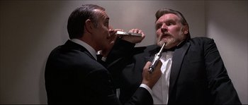 Movie still from “Never Say Never Again” (1983), directed by Irvin Kershner – Two men in tuxedos and one is holding an electric razor in his mouth; Medium shot, Low angle