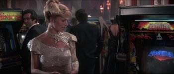 Movie still from “Never Say Never Again” (1983), directed by Irvin Kershner – A woman in a dress standing next to a man; Medium shot, Over the shoulder angle