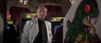 Movie still from “Never Say Never Again” (1983), directed by Irvin Kershner – A man in a white jacket standing in front of a tv; Medium shot, Low angle