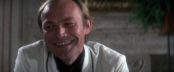 Movie still from “Never Say Never Again” (1983), directed by Irvin Kershner – A person wearing a shirt and tie smiling; Close Up shot, Low angle