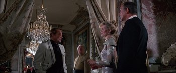 Movie still from “Never Say Never Again” (1983), directed by Irvin Kershner – A group of men and women standing in a room; Medium shot, Over the shoulder angle