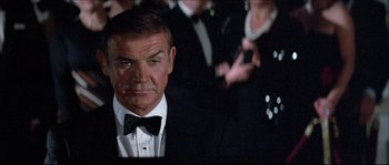 Movie still from “Never Say Never Again” (1983), directed by Irvin Kershner – A man in a suit and bow - tie looking at the camera; Close Up shot, Over the shoulder angle