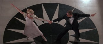 Movie still from “Never Say Never Again” (1983), directed by Irvin Kershner – A man and a woman are dancing in front of a black and white background; Wide shot, Overhead angle
