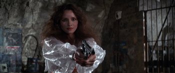 Movie still from “Never Say Never Again” (1983), directed by Irvin Kershner – A woman holding a gun while standing in front of a wall; Close Up shot, Low angle