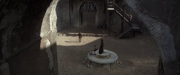 Movie still from “Never Say Never Again” (1983), directed by Irvin Kershner – Two men are sitting in a courtyard with a statue; Extreme Wide shot, High angle