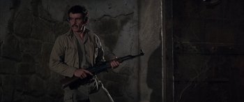 Movie still from “Never Say Never Again” (1983), directed by Irvin Kershner – A man holding a rifle in a dark room; Medium shot, Low angle