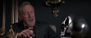 Movie still from “Never Say Never Again” (1983), directed by Irvin Kershner – An older man wearing a suit and a red bow tie; Close Up shot, Over the shoulder angle