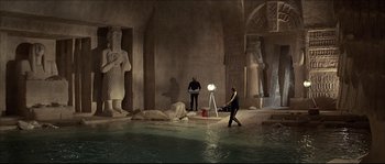 Movie still from “Never Say Never Again” (1983), directed by Irvin Kershner – Two men are standing in the water in front of statues; Extreme Wide shot, High angle