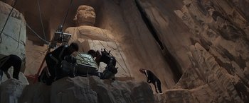 Movie still from “Never Say Never Again” (1983), directed by Irvin Kershner – A man in a black suit is standing in front of a statue; Wide shot, Low angle