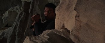 Movie still from “Never Say Never Again” (1983), directed by Irvin Kershner – A man holding a knife behind a rock wall; Medium shot, Low angle