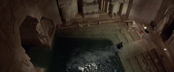 Movie still from “Never Say Never Again” (1983), directed by Irvin Kershner – A person swimming in a body of water in front of statues; Extreme Wide shot, High angle