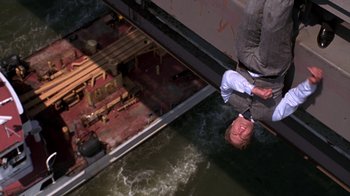 Movie still from “New Jack City” (1991), directed by Mario Van Peebles – A man in a suit hanging from a rail above water; Wide shot, Overhead angle