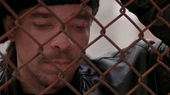 Movie still from “New Jack City” (1991), directed by Mario Van Peebles – A person behind a chain link fence; Close Up shot, High angle