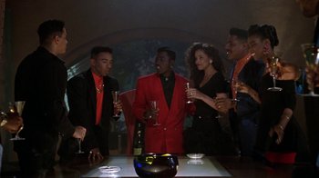 Movie still from “New Jack City” (1991), directed by Mario Van Peebles – A group of young men and women standing around a table; Medium shot, High angle